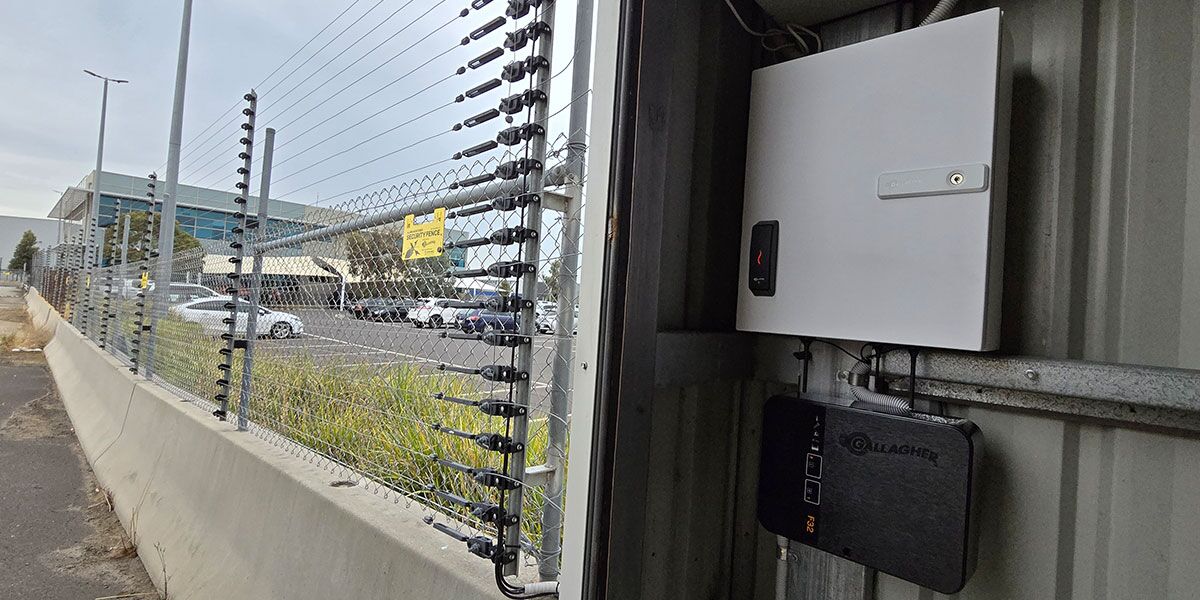 Monitored pulse fence surrounding building with a connected fence controller on a wall