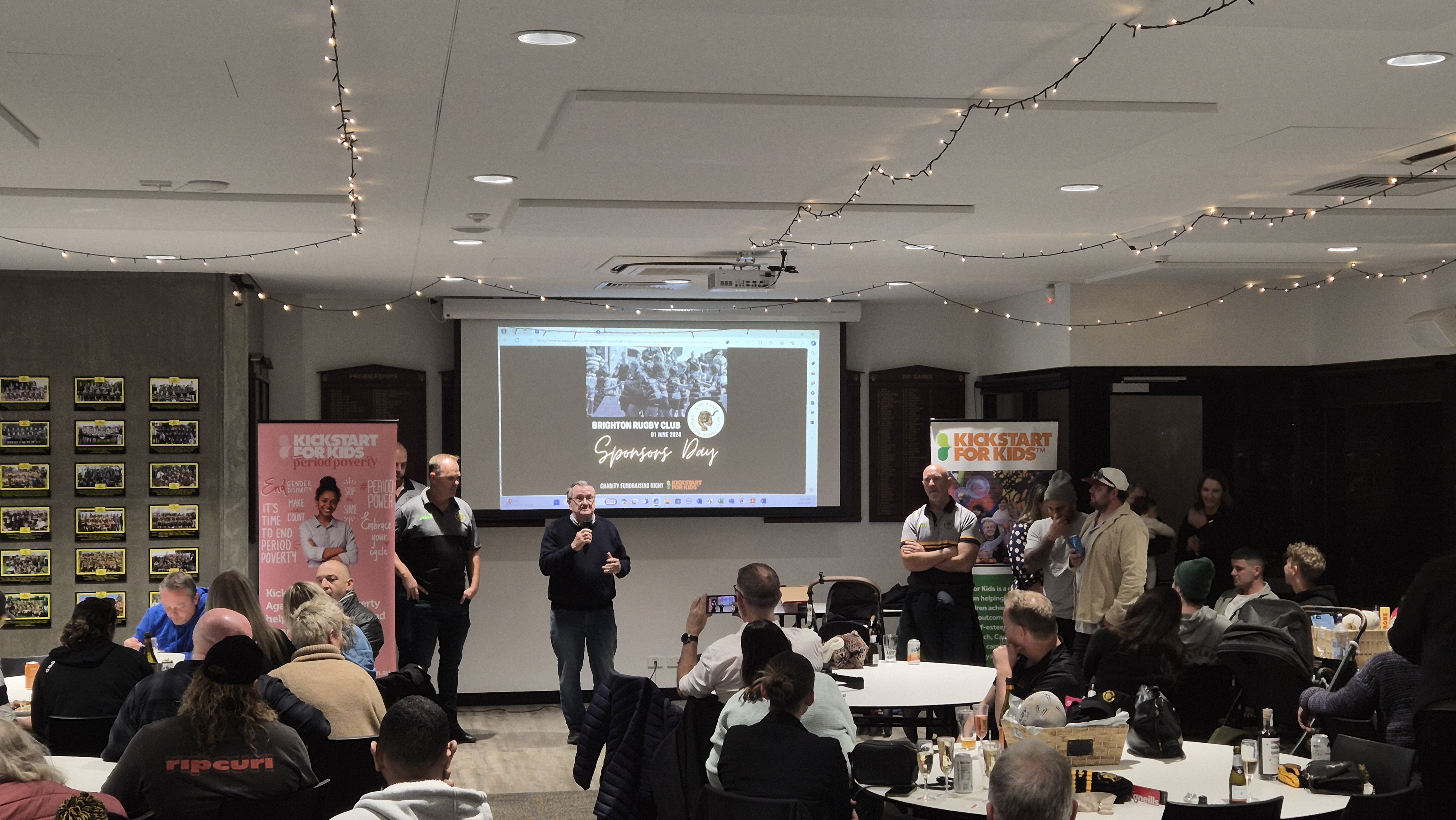 A group of individuals sitting at tables listening to two speakers at the Brighton Rugby Union Football Club sponsors day 2024