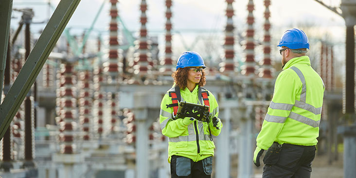 Two power plant workers standing in front of a substation